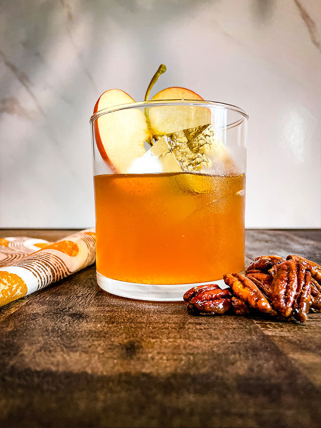 An Old Fashioned cocktail shown with an ice cube and apple slice